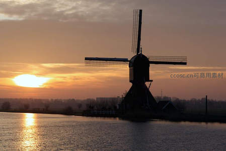夕阳下的风车剪影倒映在宁静水面