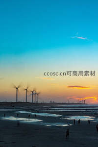 日落海滩上的风车剪影与游人