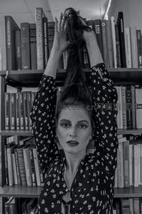 黑白影像中女子在书架前整理长发