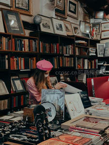 复古书店里戴粉帽的女子专注翻阅旧书
