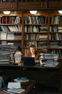 青年在书海中使用笔记本电脑学习