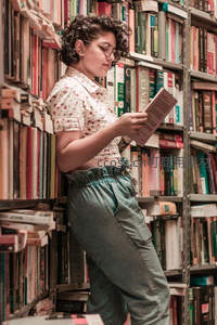 少女倚书架专注阅读，卷发眼镜尽显文艺气质