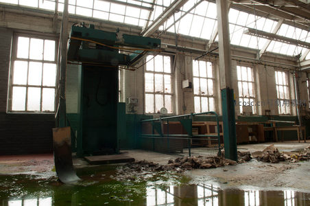 废弃工厂内部，大型机械与积水映衬工业遗迹