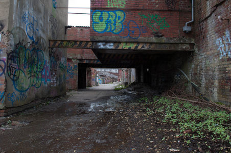 涂鸦隧道下的泥泞小径，砖墙夹道通向远方