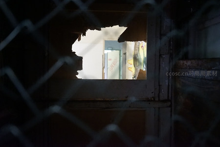 铁丝网后破窗窥见废弃房间的幽暗角落