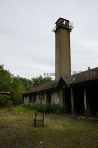 高耸烟囱旁的废弃车间，锈迹手推车静立草地