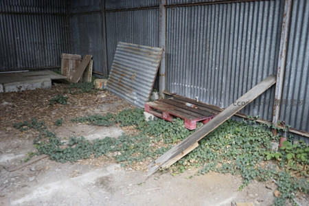 锈蚀铁皮围栏内，木托盘倾倒杂草蔓延