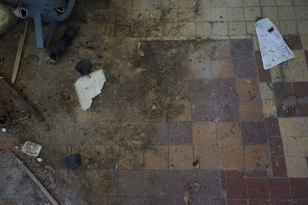 脏污的瓷砖地面残留落叶与废弃纸张