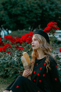 少女手捧法棍坐于玫瑰丛中微笑