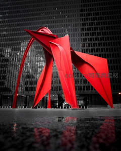 鲜红雕塑矗立都市，现代建筑倒影水洼中