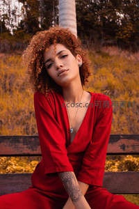 卷发女子身着红裙静坐公园长椅