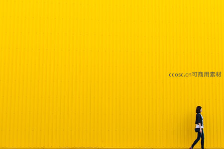 女子漫步于巨型黄色墙壁旁