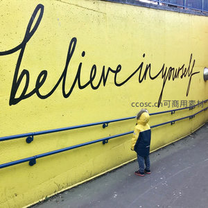 孩童仰望黄墙上的相信自己标语