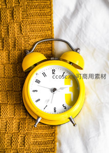 黄色闹钟静置于针织与床单之上