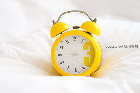 黄色复古闹钟静置于柔软床单之上