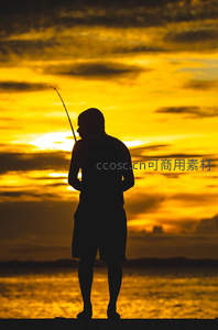 夕阳下垂钓者的剪影映照金色海面