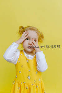 金发小女孩捂眼，黄色背景显俏皮