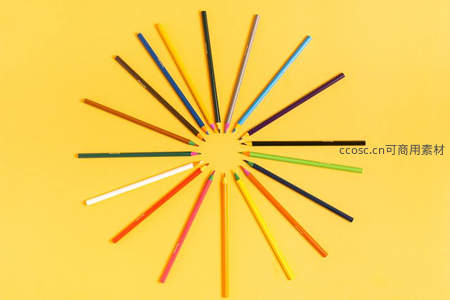 彩色铅笔在黄色背景上排列成放射状图案