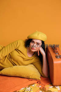 黄衣女子戴贝雷帽倚枕望镜头