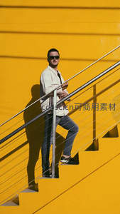 男子倚靠楼梯扶手于黄墙前