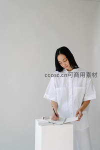 黑发女子站立书写，极简空间尽显专注