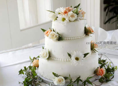 三层白色婚礼蛋糕，点缀鲜花绿叶