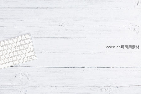 白色键盘静置于刷白木纹桌面之上