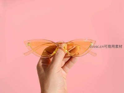 手握猫眼墨镜，粉色背景时尚特写