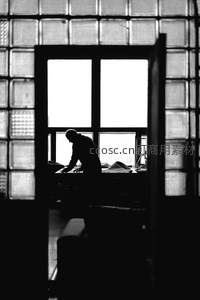 窗前剪影工作者，玻璃砖墙透出专注光芒