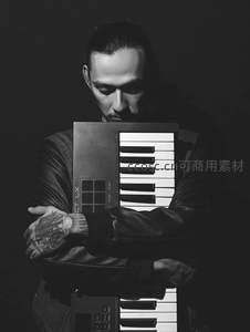 纹身男子怀抱键盘乐器沉思