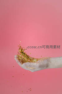 粉色背景下手掌扬起金色闪粉，动感飞扬