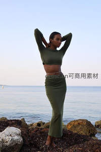 海边岩石上身着橄榄绿套装的女子