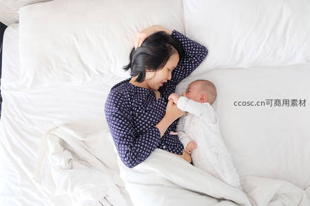 母亲床上轻抚婴儿，晨光中的温柔时光