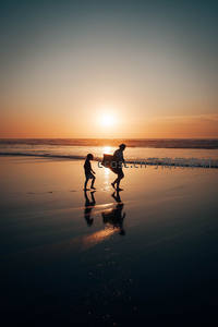 夕阳海滩剪影，父子共享冲浪时光