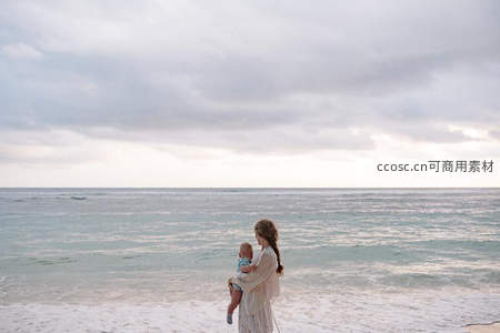 母亲抱婴伫立海边远眺云层天空