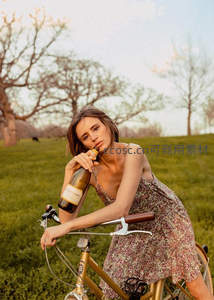 花裙女子倚靠自行车品尝酒瓶饮品