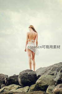 海边岩石上的白色比基尼背影