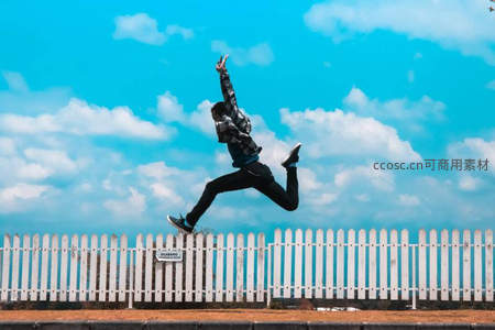 蓝天白云下，少年跃过白色栅栏，充满活力与自由。