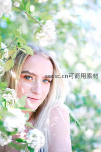 花丛中的少女，金色长发与明亮眼妆在阳光下闪耀。