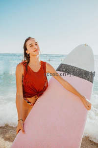 海边少女怀抱粉色冲浪板，享受阳光与海浪