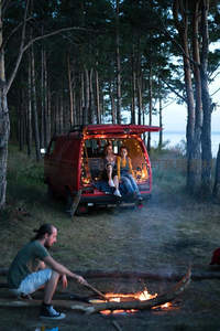 夜幕降临，红车尾灯下情侣依偎，篝火旁友人闲谈。