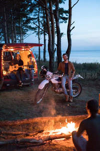 湖畔篝火旁，摩托骑士与吉他手共享黄昏露营之夜。