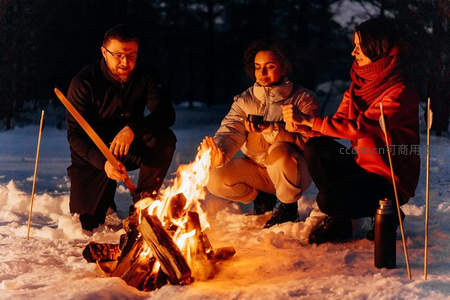 雪地篝火边三人围坐取暖聊天