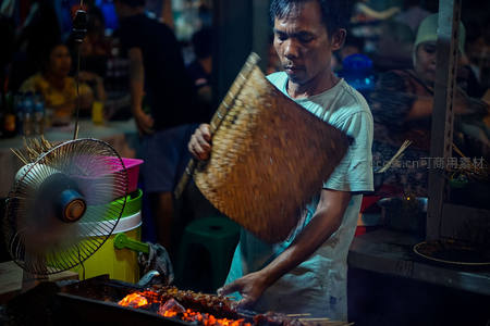 夜市摊贩用竹扇扇动炭火烤肉串