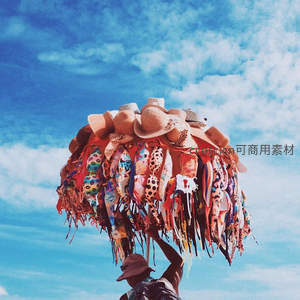 头顶花帽商贩，蓝天白云下售卖时尚配饰