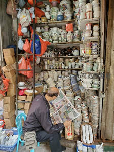 老人在陶瓷店铺前阅读报纸休憩