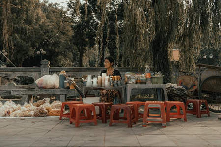 树荫下的街边小吃摊，红色塑料凳静候食客