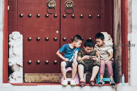 三孩童蹲坐红门前专注玩手机