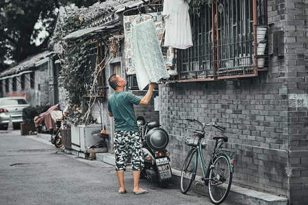 胡同里男子晾晒衣物，展现市井生活
