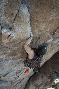 攀岩者俯身紧握岩壁，挑战极限高度